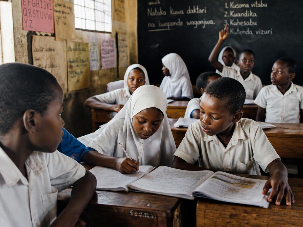 Primary school students in a bright classroom raising their hands during a lesson