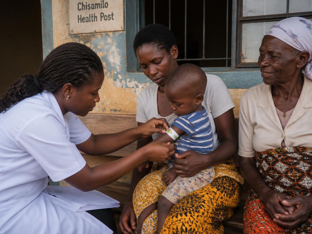 Community health worker gently examining a baby held by their mother in a clinic