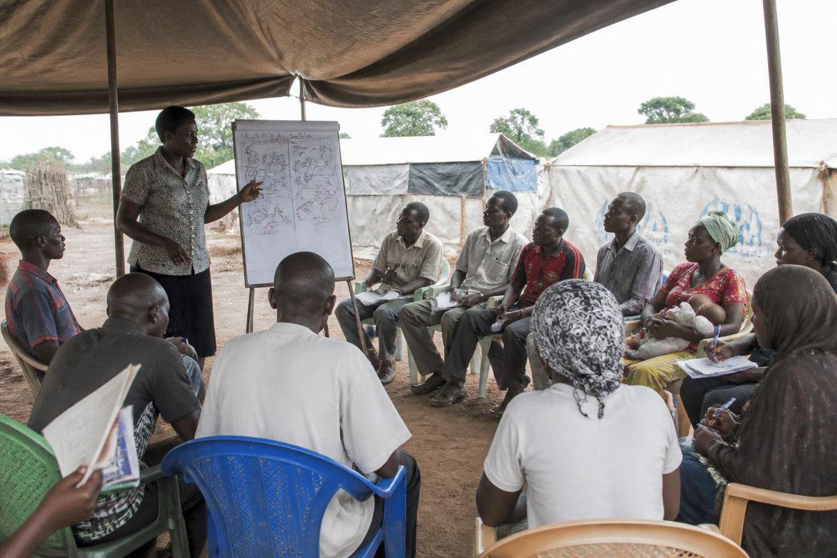 Refugee adults attending a health and protection training session with a trainer at a community centre